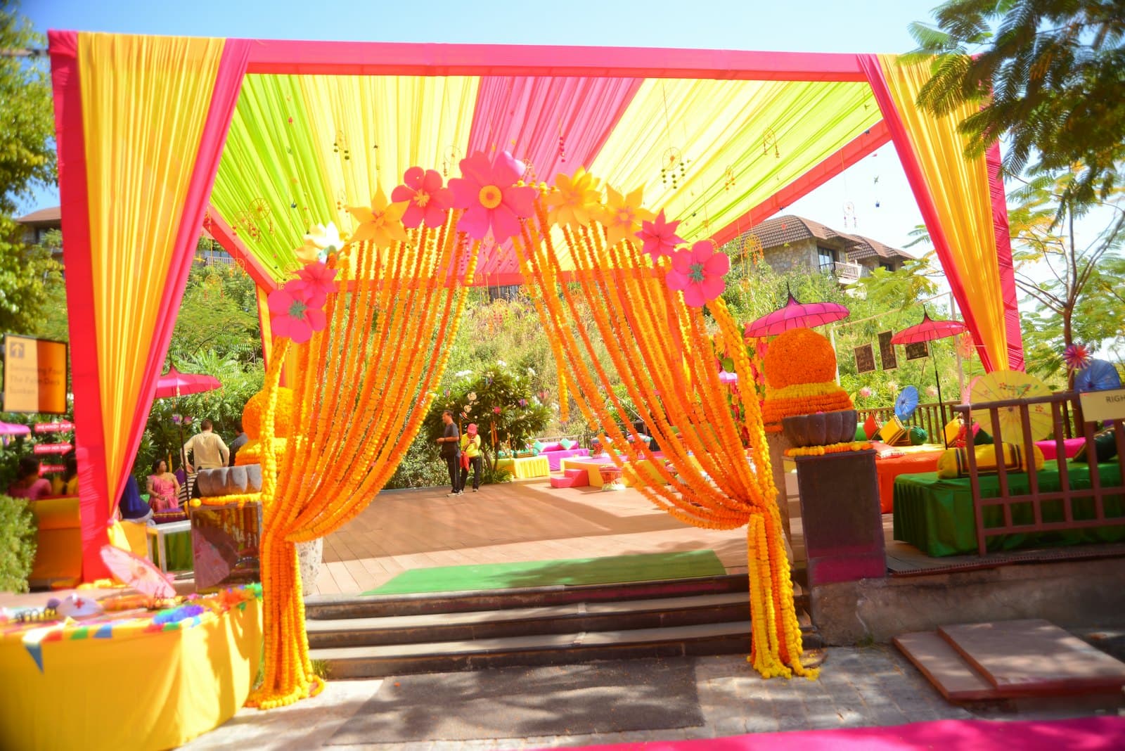 A mehndi entrance in hot pink, yellow and green drapes, hung with marigold strings and paper flowers.